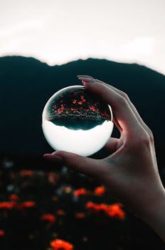 A mesmerizing crystal ball showing an inverted landscape captured in a hand.