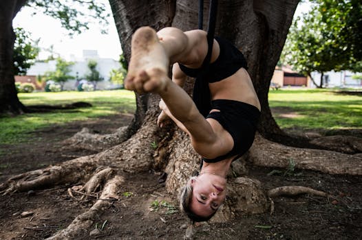 A woman performing aerial acrobatics on a rope in a serene park setting.