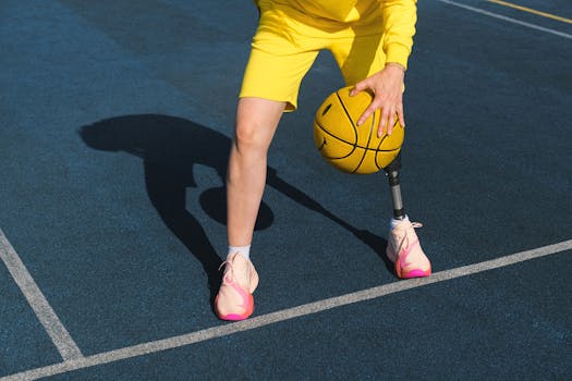 A young adult playing basketball on an outdoor court wearing sports clothing and a prosthetic leg.