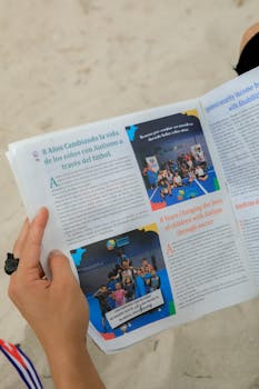 Close-up of hands holding a magazine about autism support through soccer on a sandy beach.